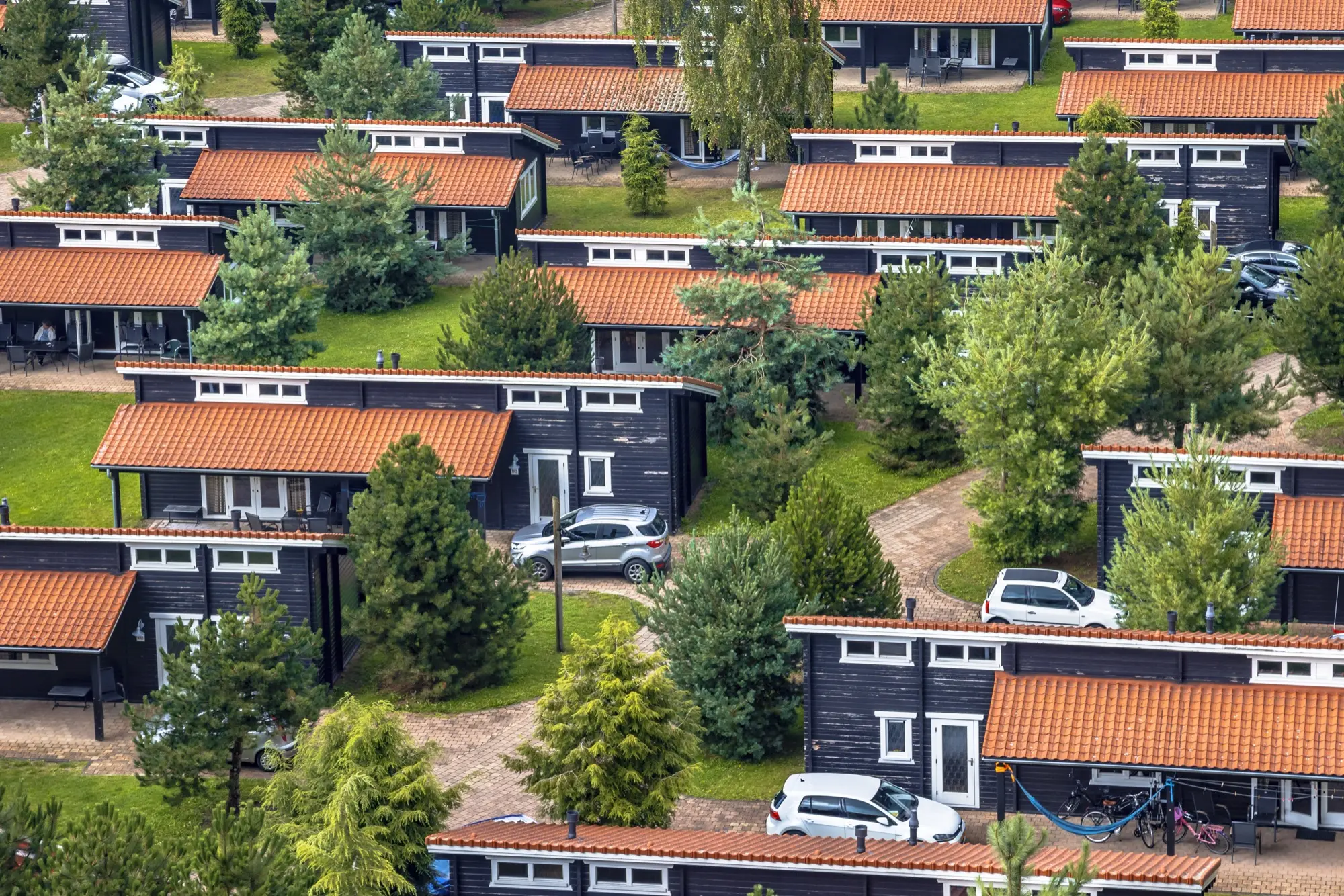 Rijen houten vakantiechalets met oranje daken en groen op een vakantiepark