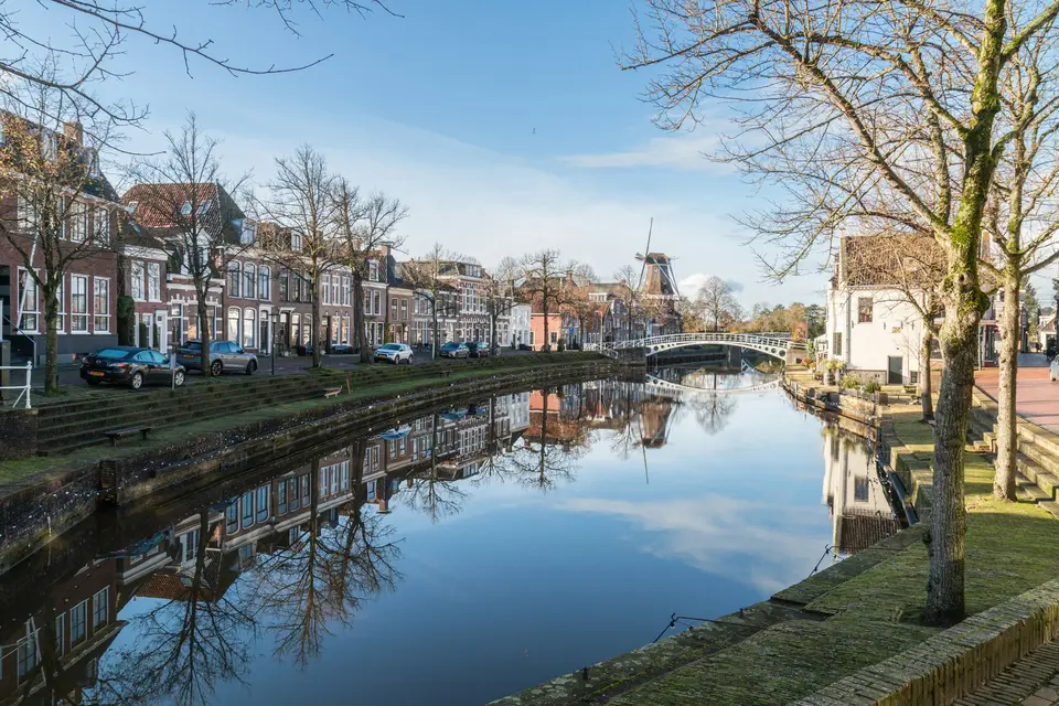 Historische gracht in Dokkum in de winter, met de gevelrij en de molen weerspiegeld in het stille water