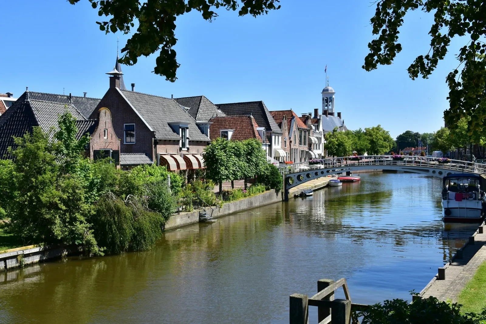 Zomerse gracht in de binnenstad van Dokkum met trapgevels langs de kade en de witte boogbrug op de achtergrond