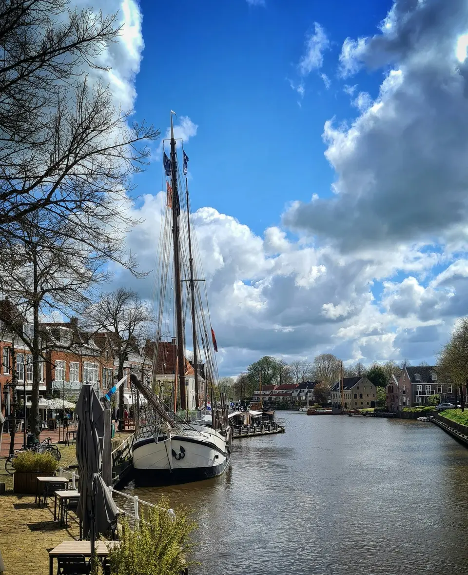 Historisch zeilschip afgemeerd aan de kade in het centrum van Dokkum, met de terrassen langs het water
